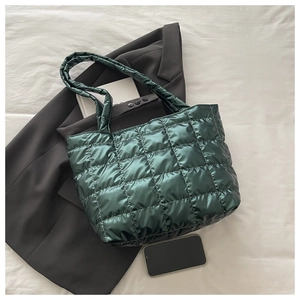 Detail of dark green quilted tote bag with metallic luster finish on a white fabric base