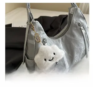 Close-up of white plush cloud charm with smiley face and gold buckle on grey bag