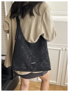 Detailed view of the large black hobo bag in suede texture worn by a model in a minimal room