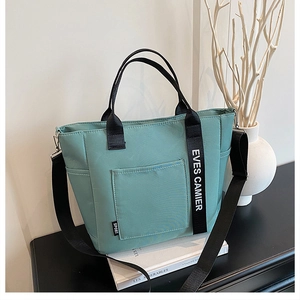 Detail of teal canvas lunch tote with black straps and side sport label on a desk