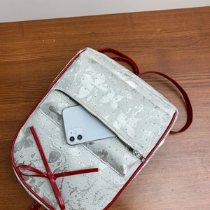 Detail view of silver backpack with red bow and studs, showing phone in front pocket