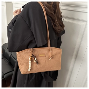 Close-up of brown suede tote bag with wooden bead charm and thin knotted shoulder strap