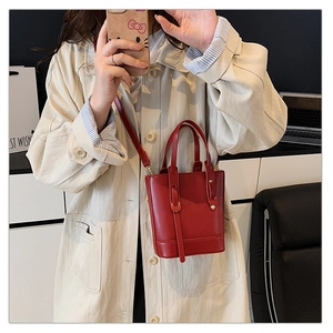 Close-up of a red leather bucket bag with top handles and a golden metal hardware finish