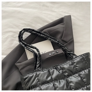 Close-up of black quilted puffer tote bag with glossy finish on grey blazer background
