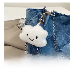 Close-up of white plush cloud charm with smiley face on denim tote bag detail
