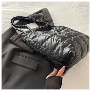 Detail view of black quilted puffer tote bag on grey blazer with soft nylon texture