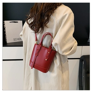 Sac seau rouge avec anses et détails dorés porté par un mannequin pour l'échelle
