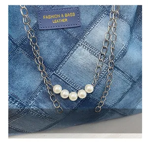 Detail of denim texture tote bag with silver chains, pearls and fashion leather label