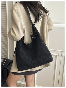 Detailed view of black suede tote bag with knotted strap and small flap accessory