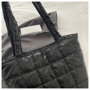 Close-up of black quilted tote bag with puffy padded texture and wide shoulder strap
