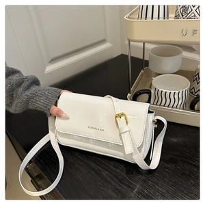 Detail of white glossy lacquer shoulder bag with gold branding and adjustable strap