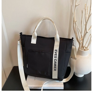 Detail of a black nylon lunch tote with wide lettered straps and front storage pocket