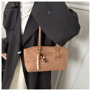 Detail of a brown suede tote bag featuring a Fashion label and vintage wooden bead charm