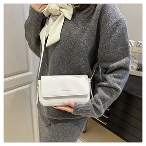 White glossy patent leather square bag with gold hardware shown on a female model