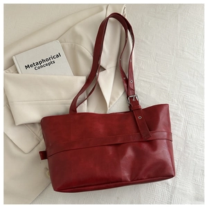 Close-up of a burgundy leather tote bag with silver metal buckle and decorative strap