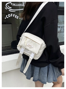 Detail of off-white waterproof nylon crossbody bag with functional zip pockets and buckles