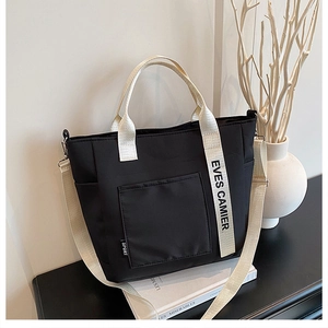 Detail of black canvas tote bag with adjustable branded shoulder strap and front pocket