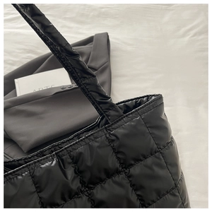 Detailed close-up of black quilted tote bag with glossy nylon texture and padded handles