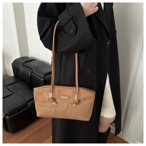 Close-up of brown suede hobo bag with knot detail and fashion label on a leather sofa