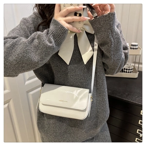 Close-up of minimalist pearl white patent leather crossbody bag with gold logo