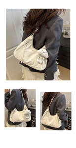 Detail of off-white crescent shoulder bag with silver zippers and plush cloud charm accessory