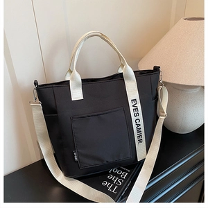 Detail of black canvas tote bag showing wide woven straps and logo side label detail