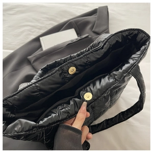 Detail of magnetic buckle closure on a black quilted puffy tote bag for women