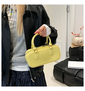 Detail of a bright yellow cylindrical pillow bag with dual handles and smooth leather texture