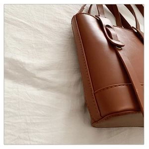 Détail d'un sac à main en cuir marron montrant des coutures précises et une texture lisse