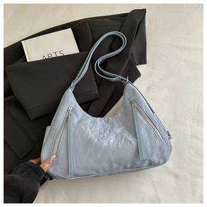Detail of light blue wrinkled nylon tote bag with silver zippers on neutral fabric