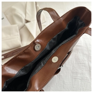 Detail of silver magnetic snaps and black lining on brown faux leather tote bag