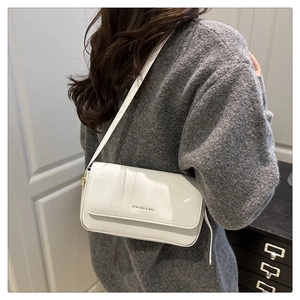 Close-up of a white patent leather shoulder bag with logo detail on a female model