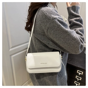 Close-up of white glossy patent leather bag with gold hardware and magnetic flap closure