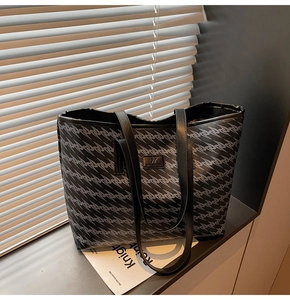 Detail of large tote bag with geometric print and leather straps near a window shadow