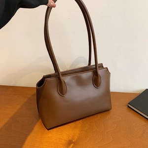 Minimalist brown matte tote bag with slim shoulder straps shown in a warm indoor setting