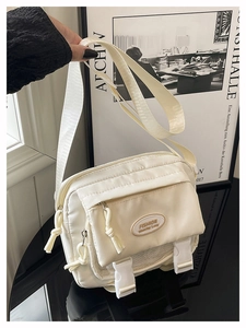 Close-up of beige nylon messenger bag showing front zipper pocket and buckle flap details
