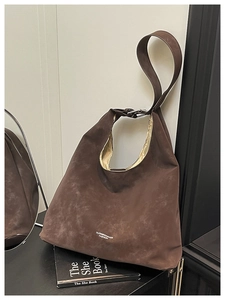 Detail of a large brown suede tote bag with logo leaning against a white wall next to a book