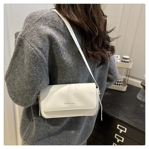 White faux leather crossbody bag with minimalist lettering shown on model's shoulder