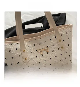 Close-up of cream tote bag featuring textured fabric and a gold bow metal accent