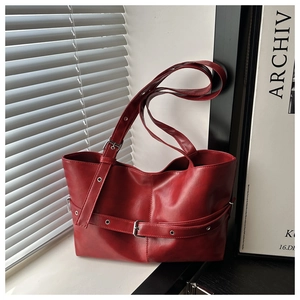 Detail view of red faux leather tote bag with metallic buckle belts and long shoulder strap