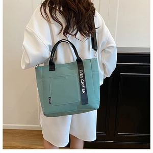 Detail of mint green tote bag featuring black woven strap and functional front pocket