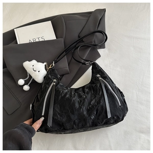 Detail of black tote bag with wrinkled texture, silver zippers, and cloud plush charm
