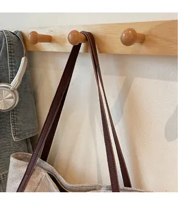 Detail of off-white canvas tote bag with brown leather strap hanging on a wooden hook