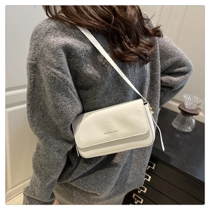 Close-up of a white patent leather shoulder bag featuring a sleek minimalist buckle design