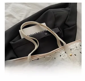 Close-up of white jacquard tote bag with bow pendant, gold rivets, and detailed texture
