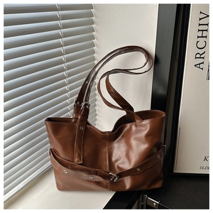 Close-up of brown leather tote bag detailing metallic buckle and textured surface