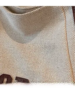 Macro detail of beige canvas texture with brown leather stitched logo on a tote bag
