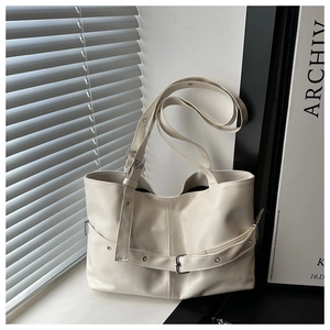 Detail of cream white tote bag featuring decorative eyelet straps and silver hardware