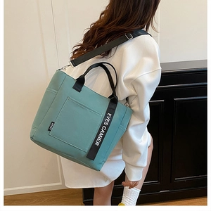 Detail of mint green tote bag with black straps and EVES CAMIER printed text