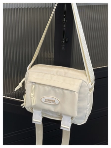 Detail of cream nylon crossbody bag featuring buckle pockets and fashion label